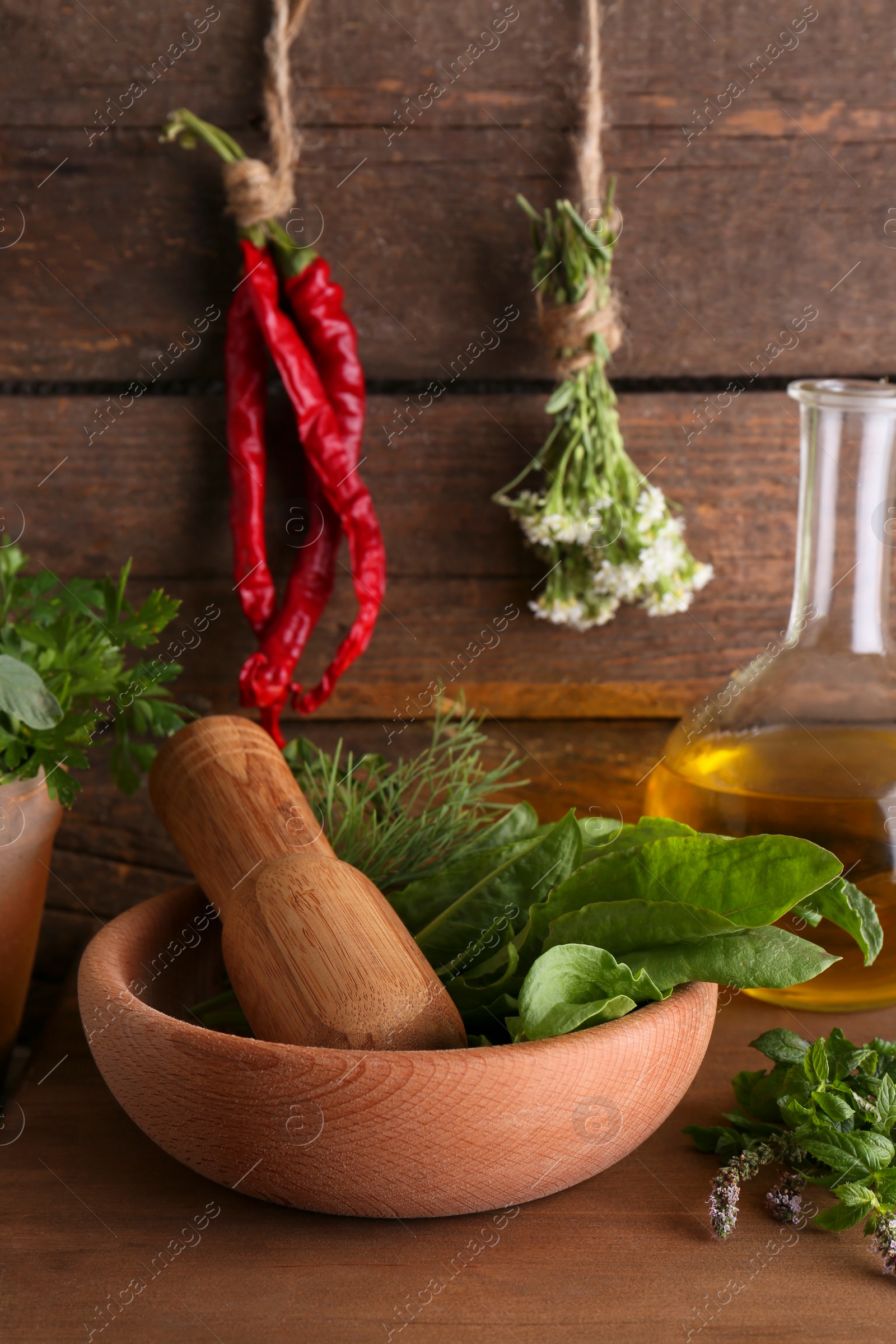 Photo of Mortar with pestle, fresh green herbs and oil on wooden table