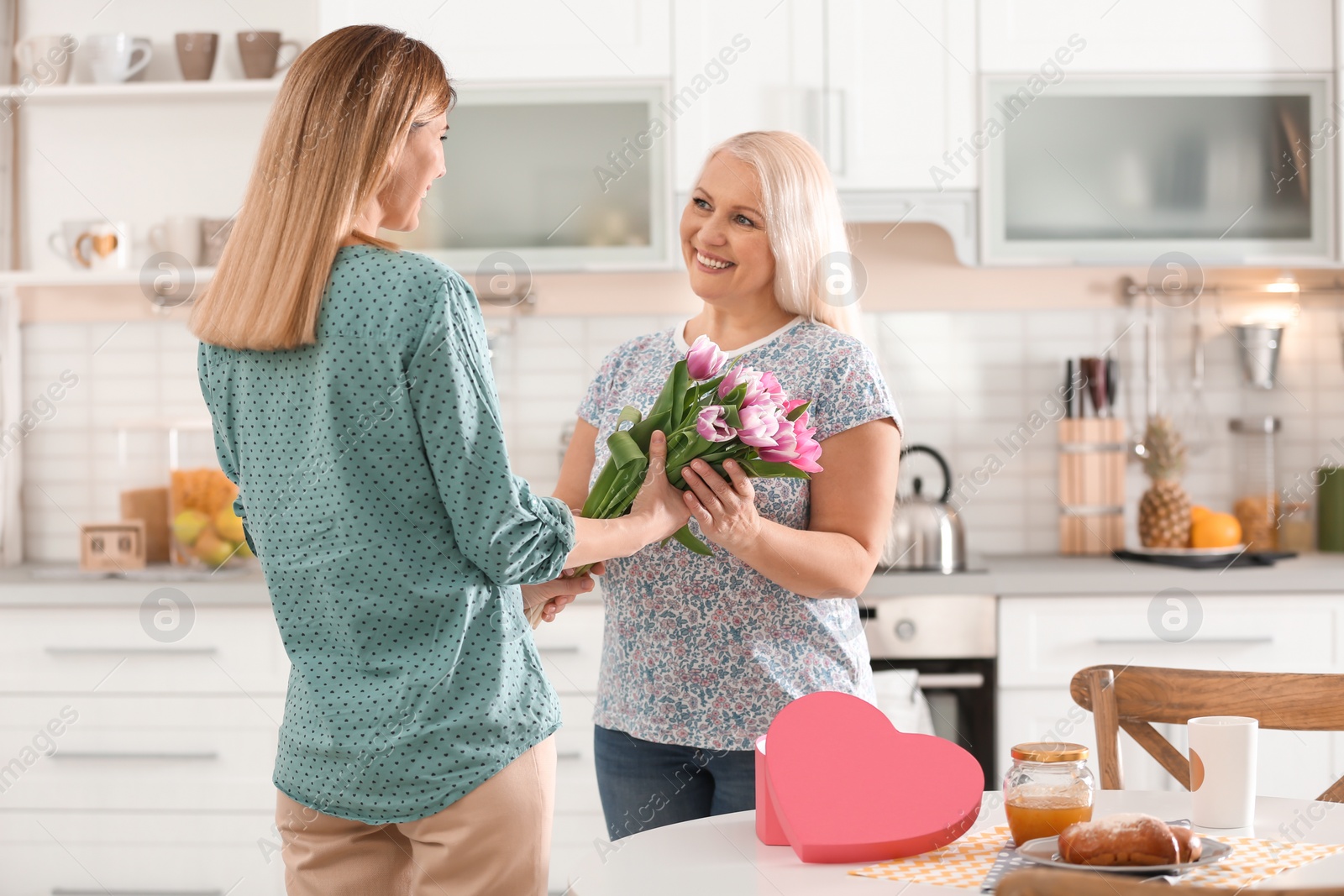 Photo of Daughter congratulating happy mature woman on Mother's Day at home