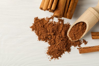 Dry aromatic cinnamon sticks, powder and scoop on white wooden table, flat lay. Space for text