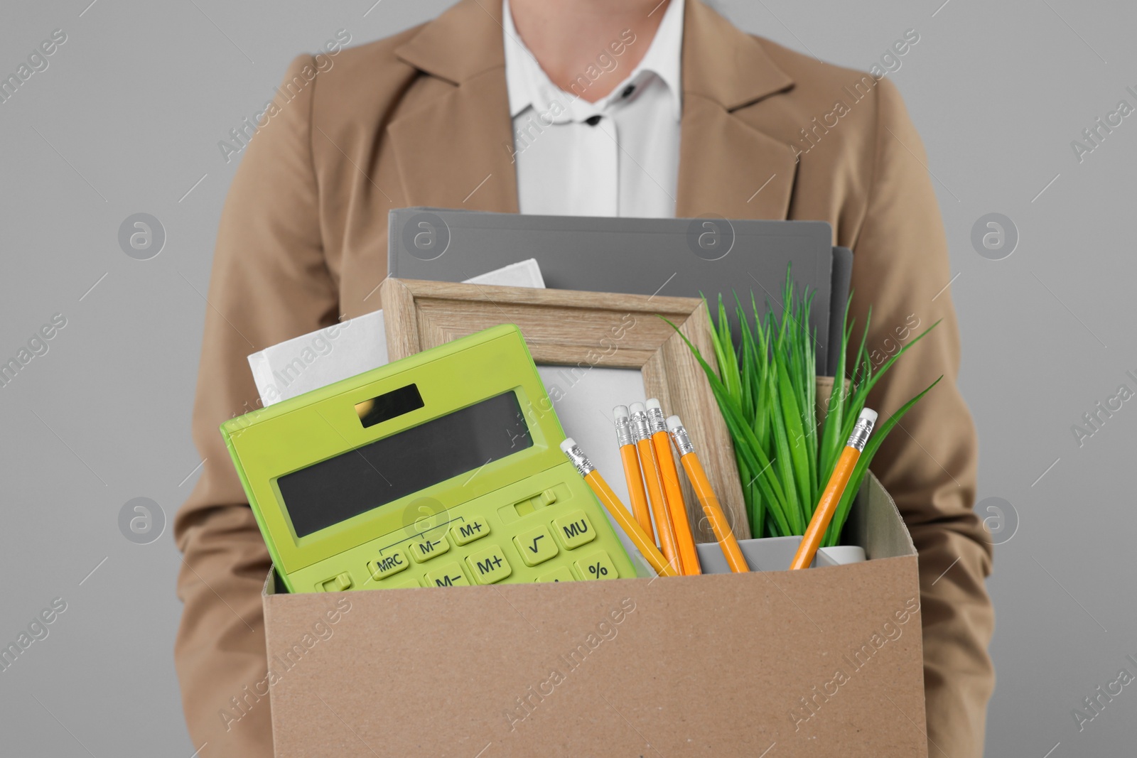Photo of Unemployed woman holding box with personal office belongings on grey background, closeup