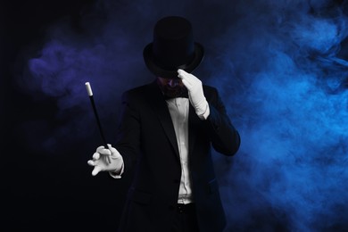 Magician holding wand in smoke on dark background