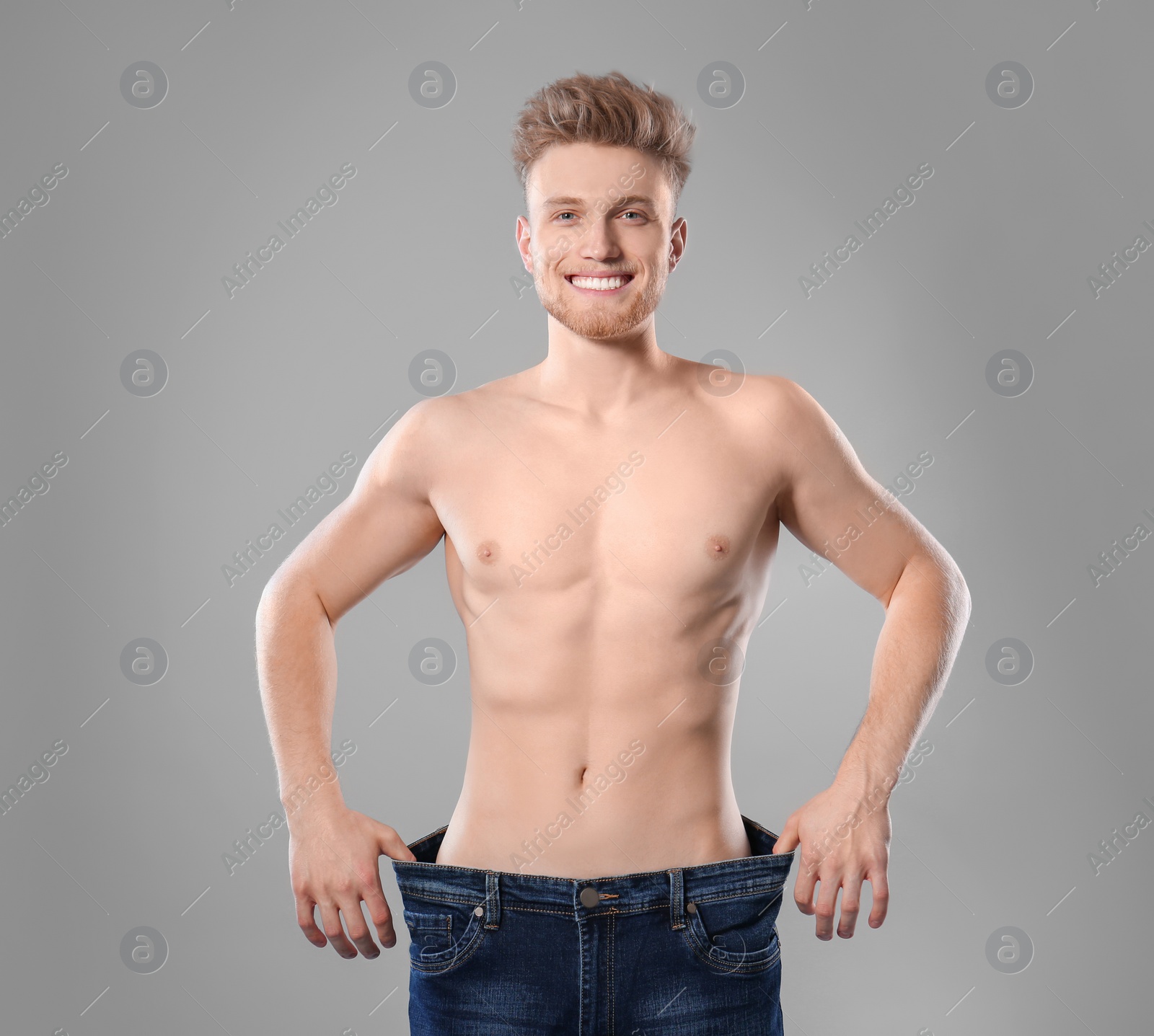 Photo of Young man with slim body in old big size jeans on grey background