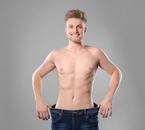 Photo of Young man with slim body in old big size jeans on grey background