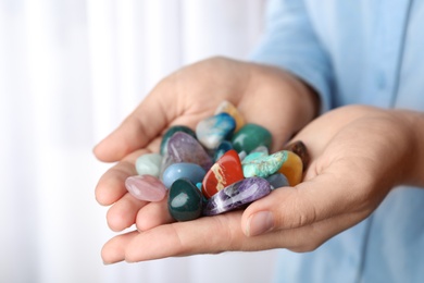 Photo of Woman holding pile of different gemstones indoors, closeup