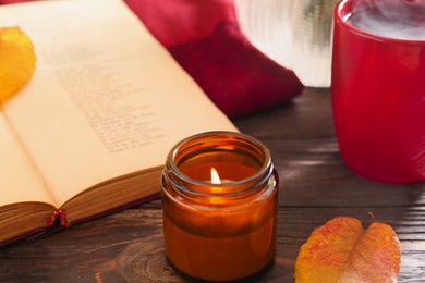 Photo of Burning scented candle, cup of tea and book on wooden table. Autumn atmosphere