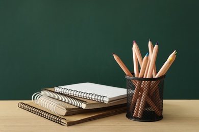 Photo of Different school stationery on wooden table near green chalkboard. Back to school