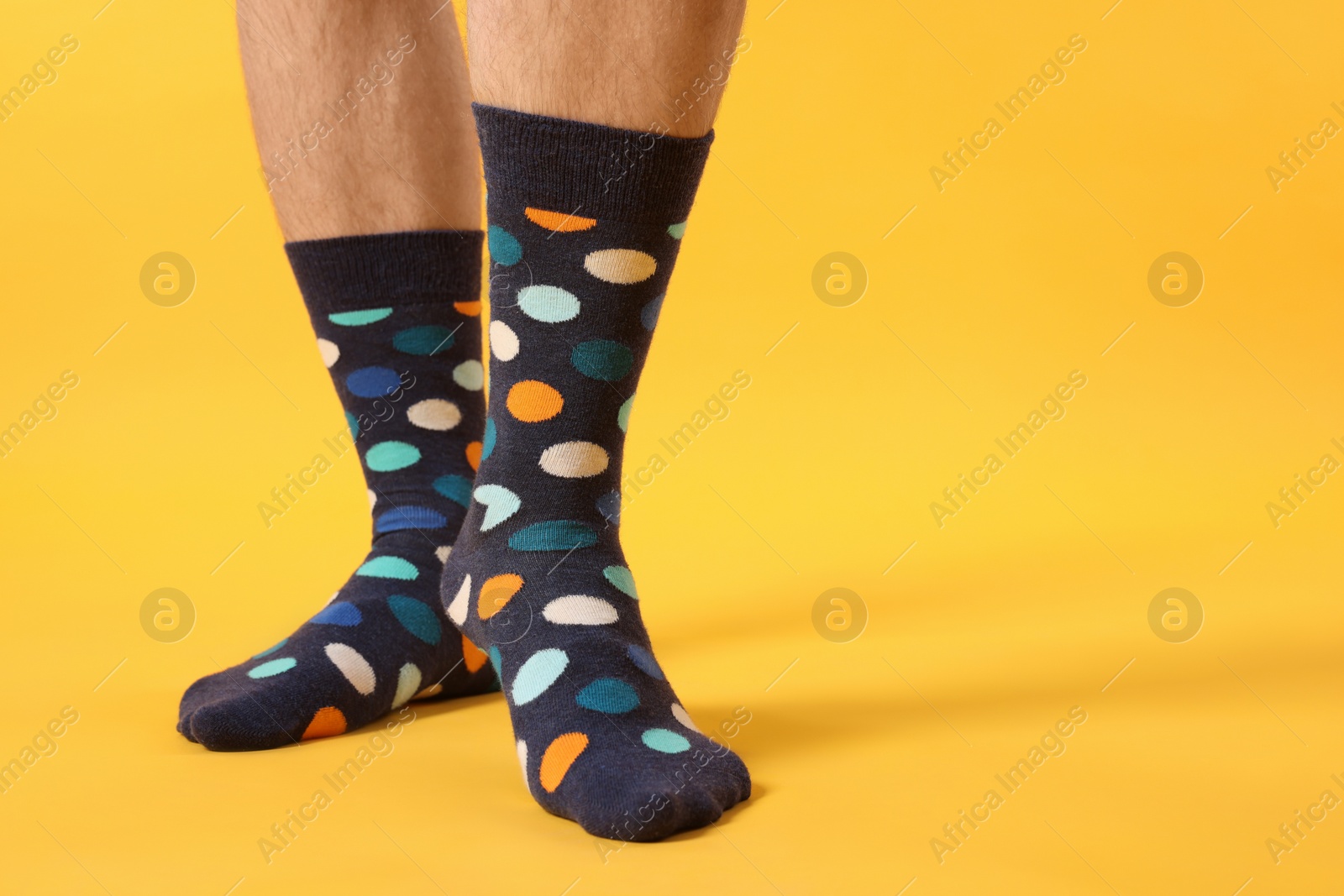 Photo of Man in stylish colorful socks on yellow background, closeup. Space for text