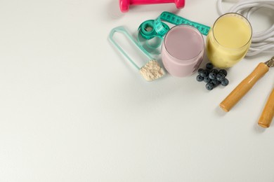 Photo of Tasty shakes, sports equipment, measuring tape and powder on white table, flat lay with space for text. Weight loss