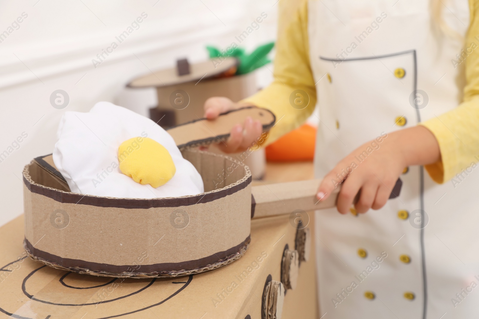 Photo of Little girl playing with toy cardboard kitchen indoors, closeup