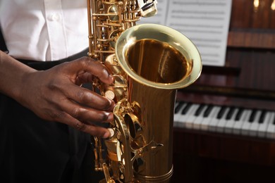 Photo of African-American man playing saxophone indoors, closeup. Talented musician
