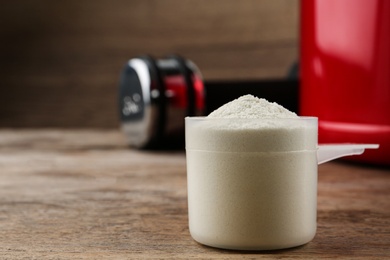 Photo of Measuring scoop of protein powder on wooden table, closeup. Space for text