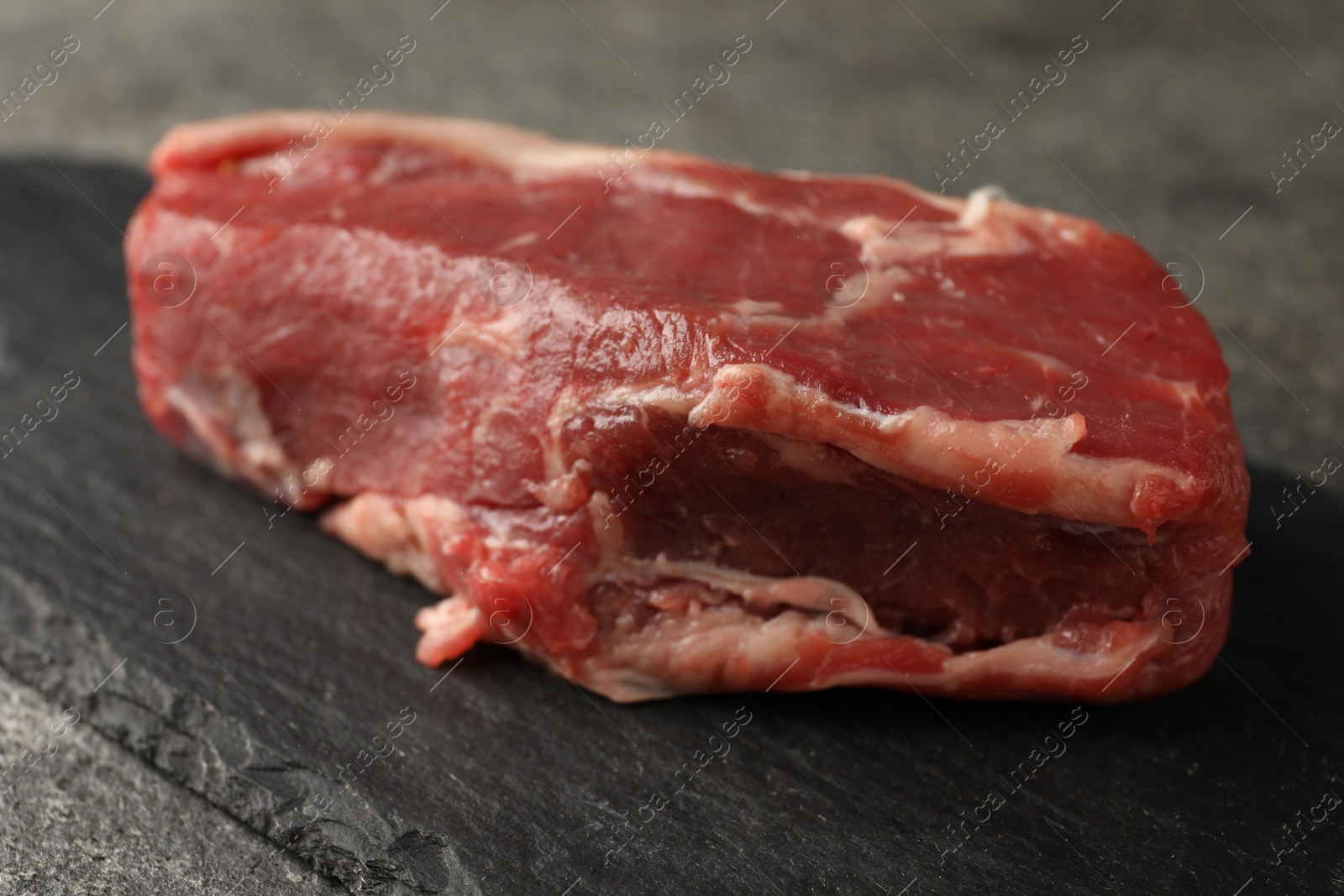 Photo of Piece of raw beef meat on grey table, closeup