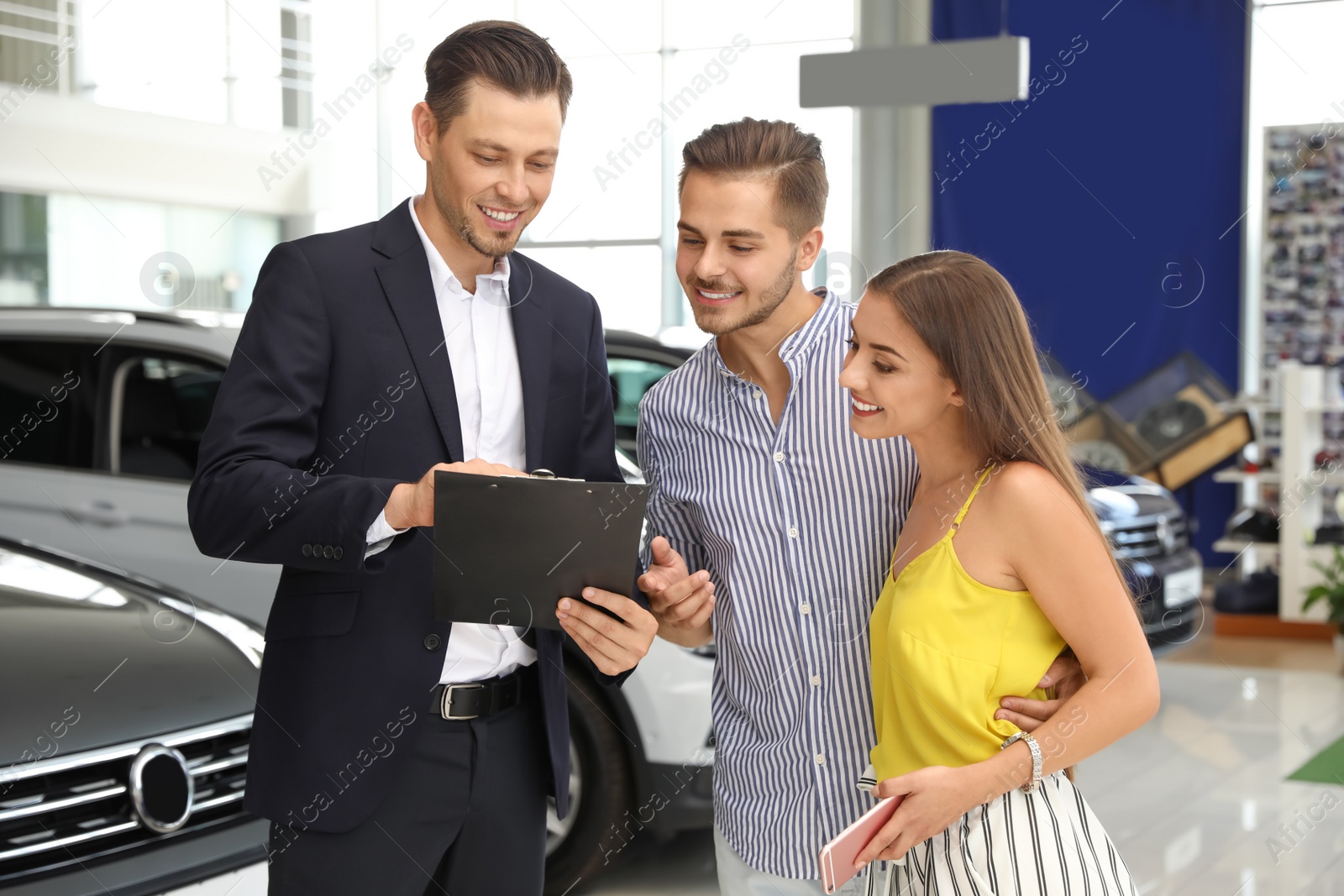Photo of Young couple choosing new car with salesman in salon