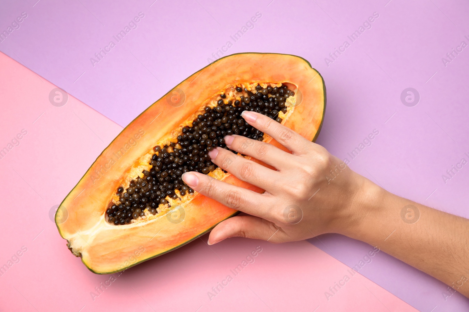 Photo of Young woman touching half of papaya on color background, above view. Sex concept