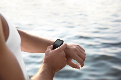Man checking fitness tracker after training near river, closeup