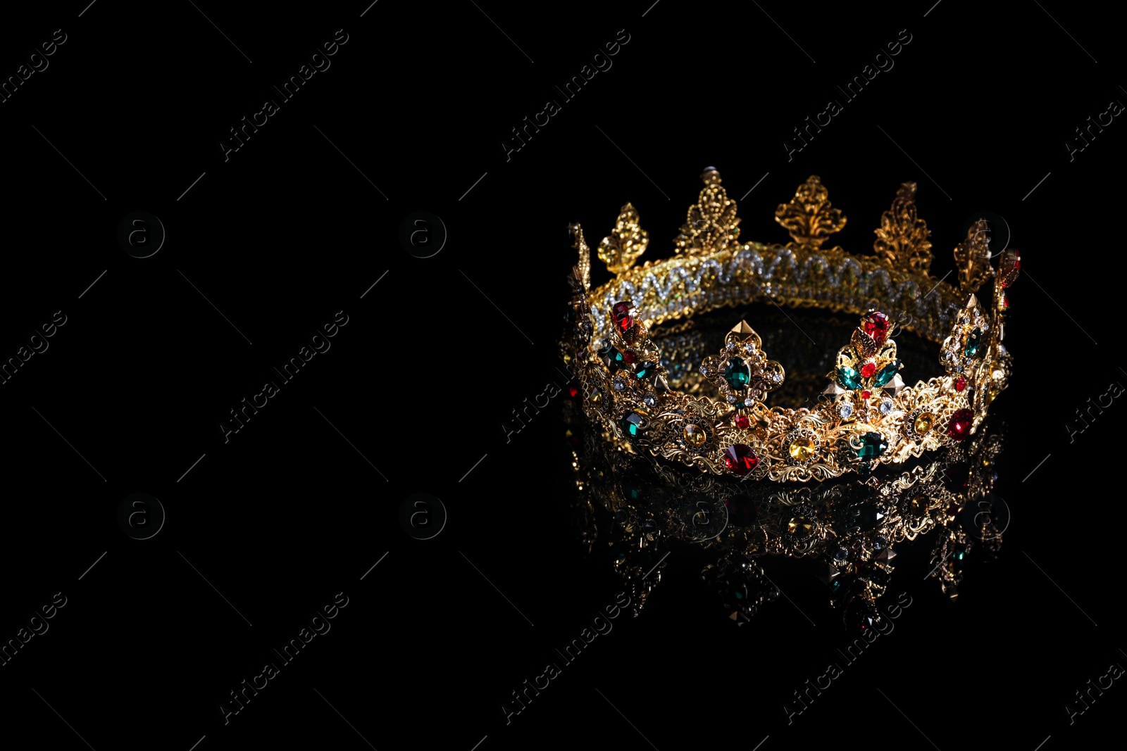 Photo of Beautiful golden crown with gems on dark mirror surface. Space for text