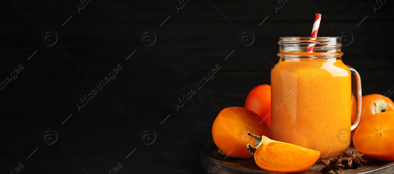 Image of Tasty persimmon smoothie with straw and fresh fruits on table against black background, space for text. Banner design