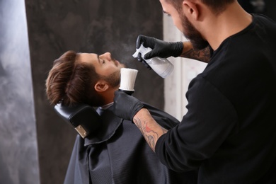 Photo of Professional hairdresser using talcum powder to calm client's skin after shaving in barbershop