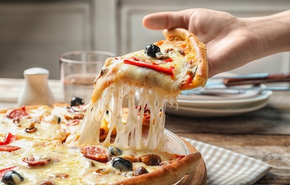 Photo of Woman holding slice of delicious hot pizza over table, closeup