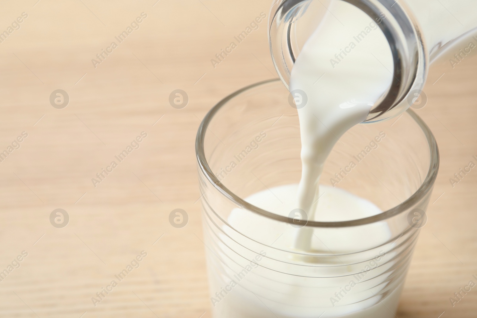 Photo of Pouring milk into glass on table, closeup. Space for text