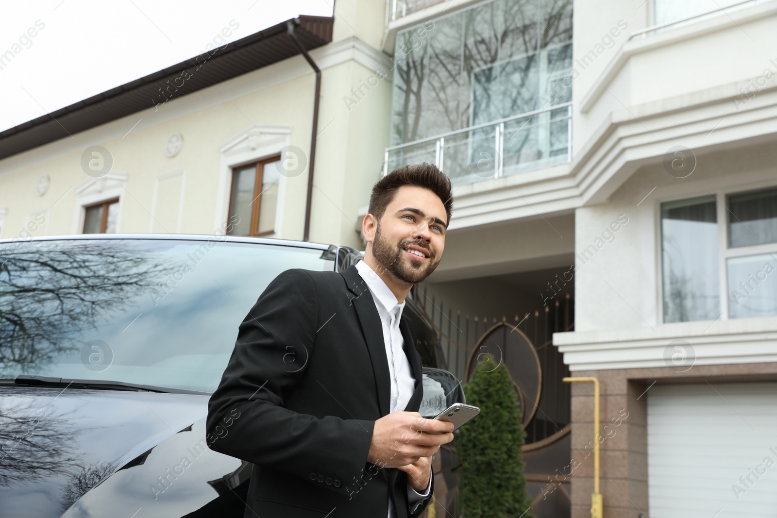 Photo of Handsome young man with smartphone near modern car outdoors