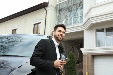 Handsome young man with smartphone near modern car outdoors