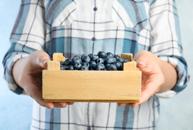 Photo of Woman holding wooden crate with fresh ripe blueberries, closeup