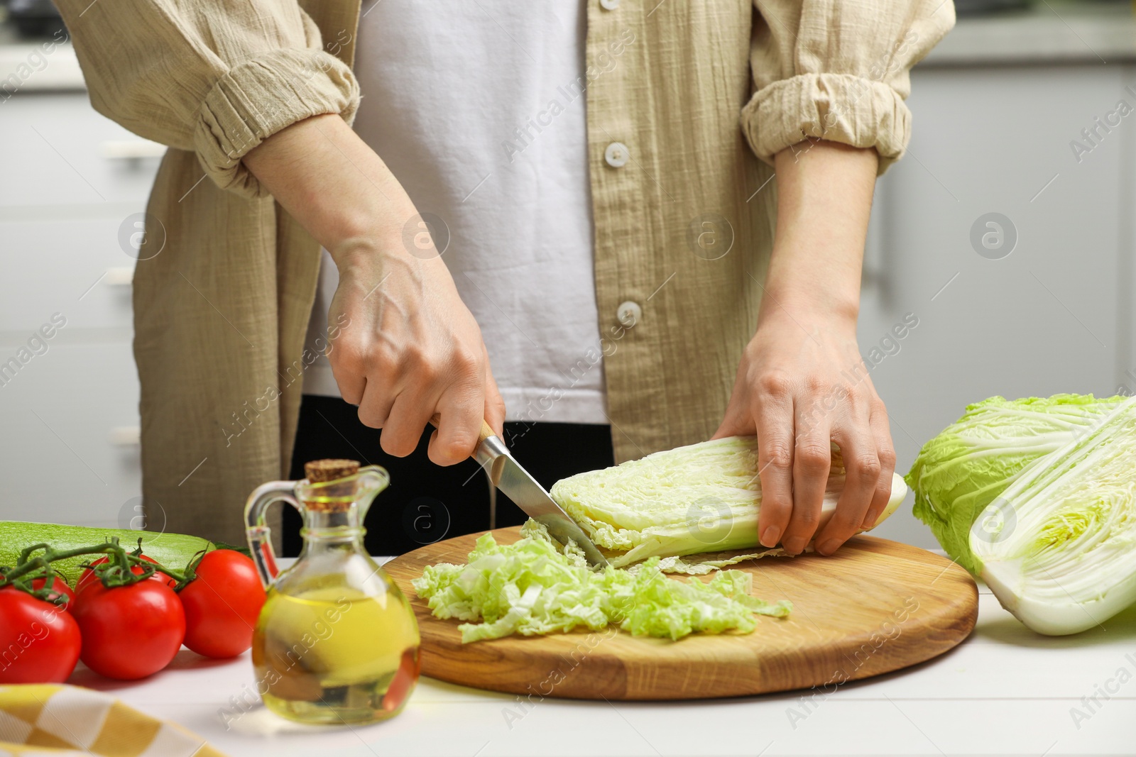 Photo of Woman cutting fresh chinese cabbage at white wooden table in kitchen, closeup