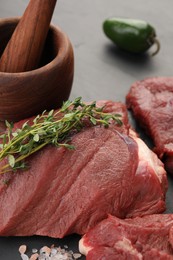 Photo of Pieces of raw beef meat, mortar with pestle, microgreens and sea salt on table, closeup