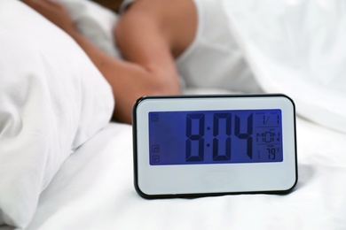 Photo of Digital alarm clock and sleepy woman in bed. Time of day