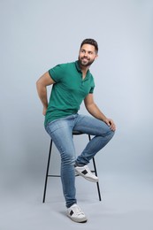 Photo of Handsome young man sitting on stool against light grey background