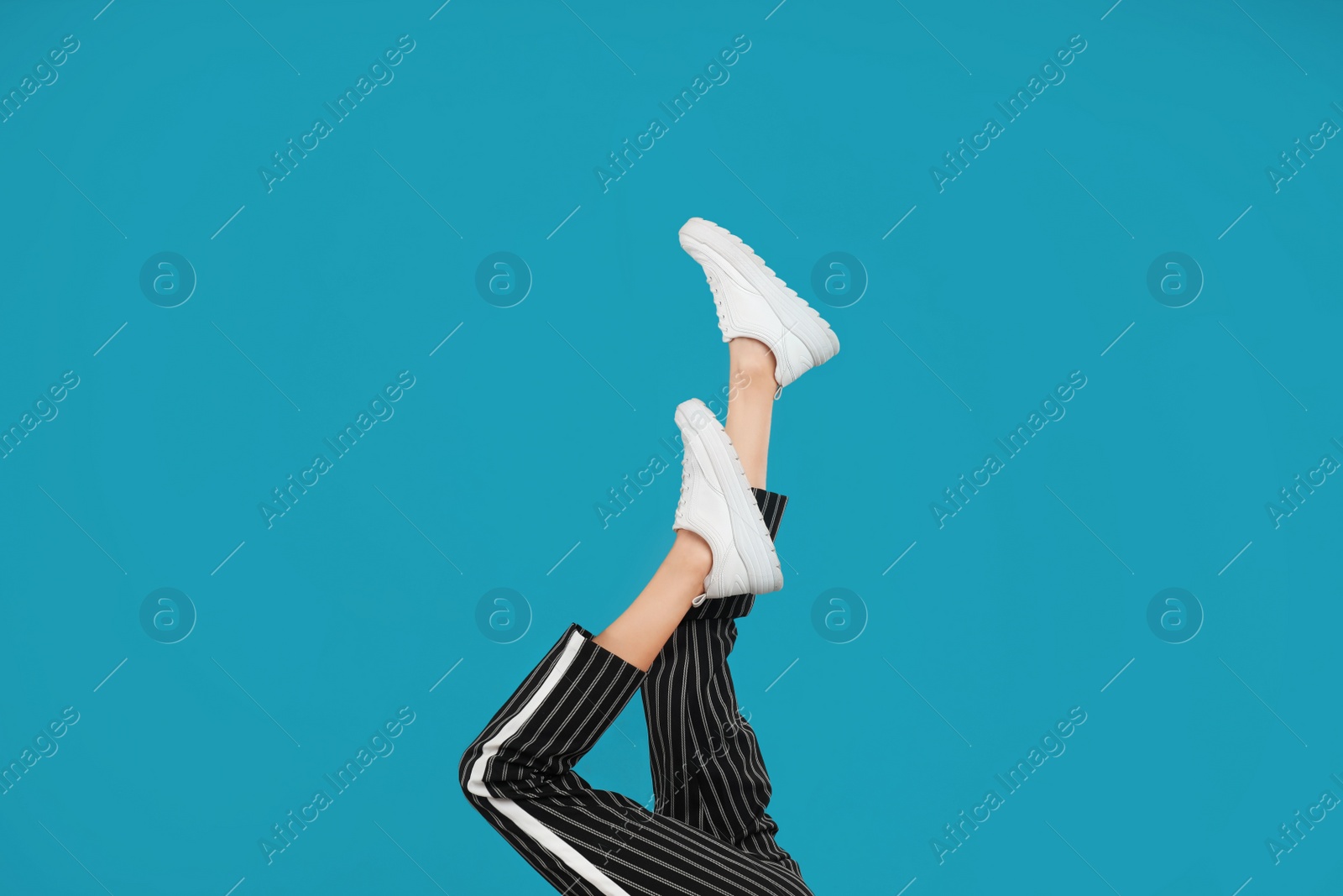 Photo of Woman in stylish sport shoes on light blue background