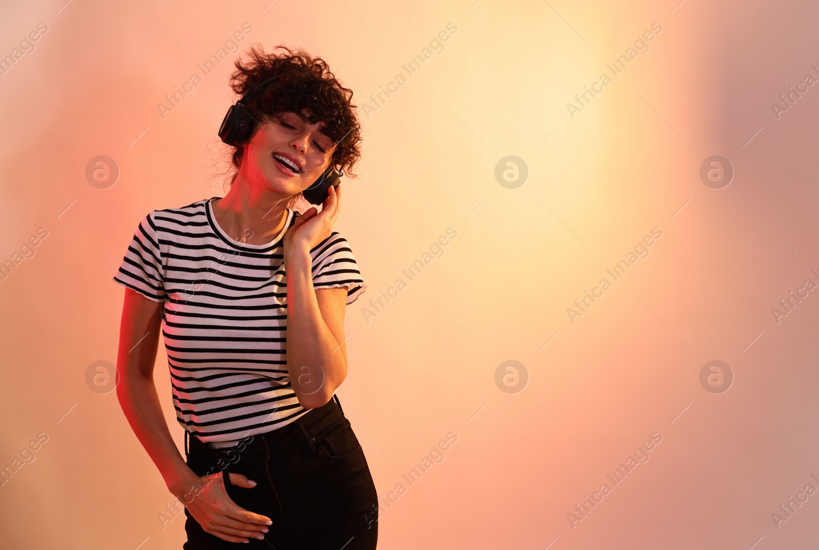 Photo of Beautiful young woman listening to music with headphones on color background in neon lights. Space for text