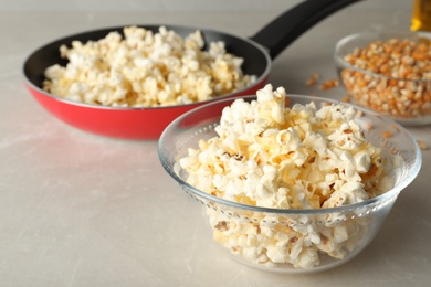 Photo of Glass bowl with tasty popcorn on grey table. Space for text