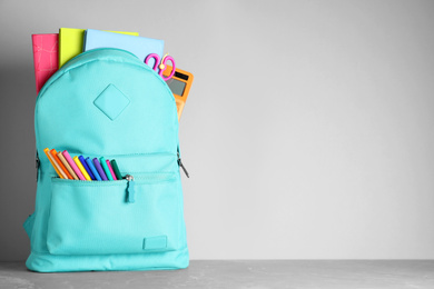 Stylish backpack with different school stationery on table against light grey background. Space for text