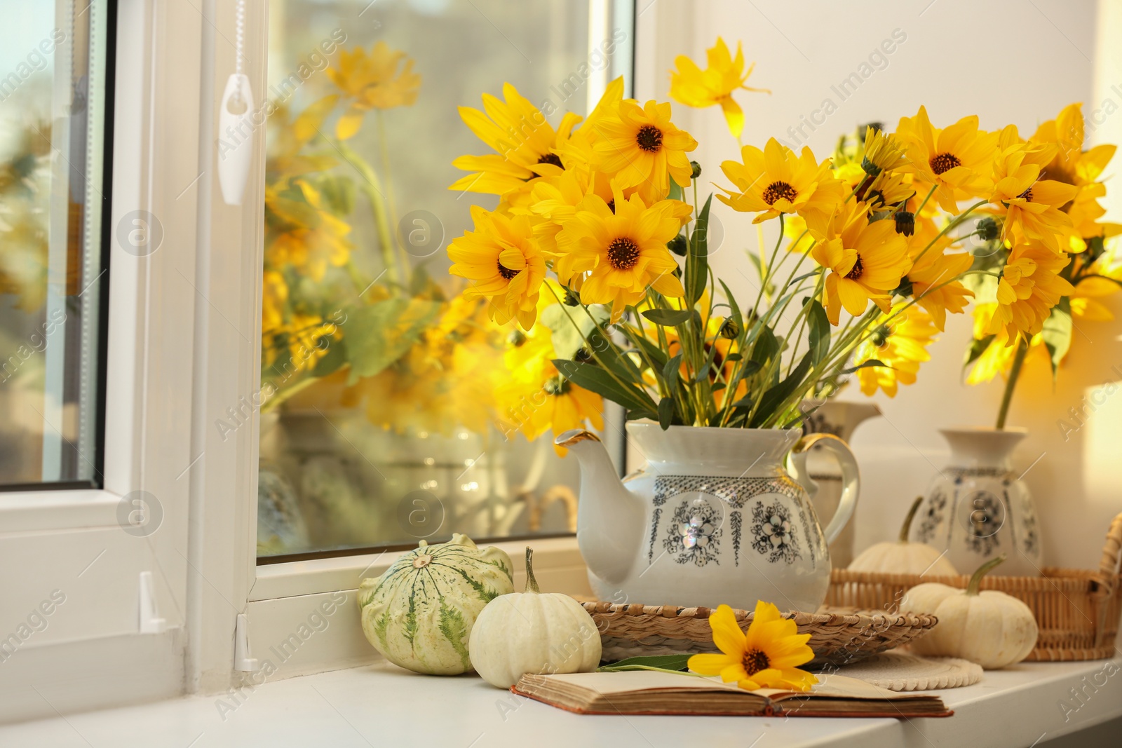 Photo of Composition with beautiful flowers, pumpkins and book on windowsill. Autumn atmosphere