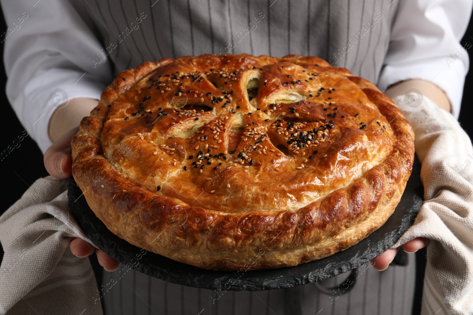 Photo of Woman holding tasty homemade pie on black background, closeup