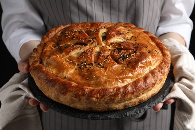 Photo of Woman holding tasty homemade pie on black background, closeup