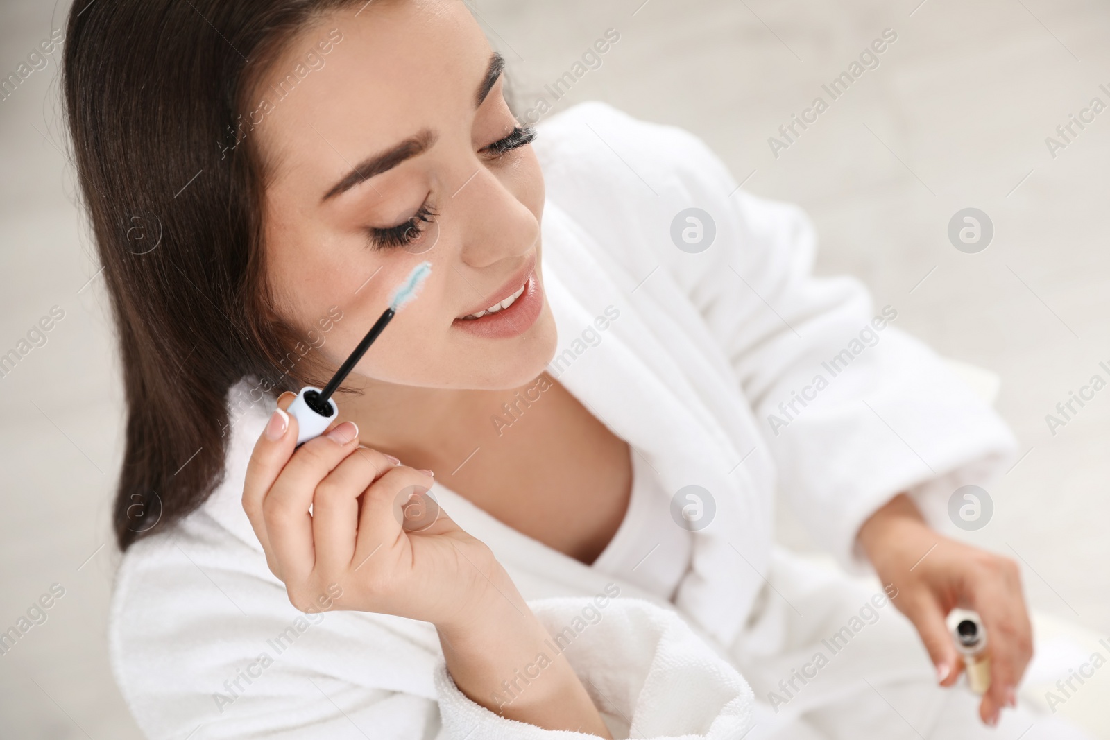 Photo of Attractive young woman applying oil onto her eyelashes indoors