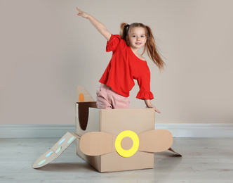 Cute little child playing with cardboard plane near beige wall