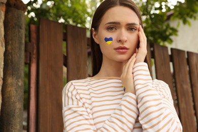 Photo of Young woman with drawing of Ukrainian flag on face outdoors