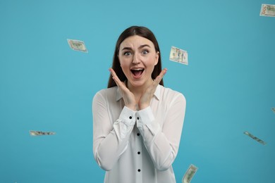 Excited woman under money shower on light blue background