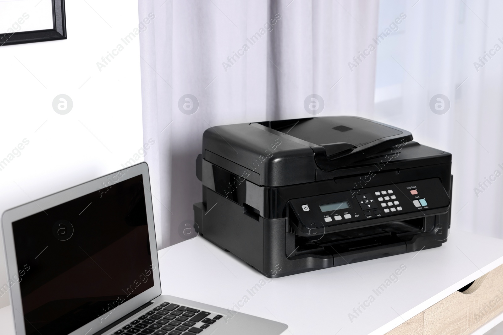 Photo of Modern printer with paper near laptop on white desk at home