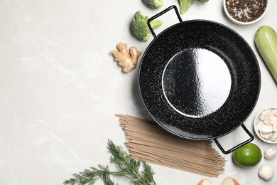 Photo of Empty iron wok surrounded by raw ingredients on light table, flat lay. Space for text