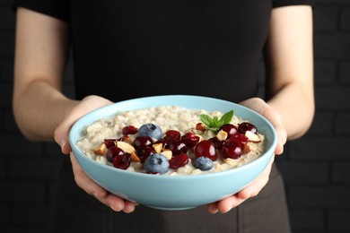 Woman holding bowl of oatmeal porridge with berries on black background, closeup