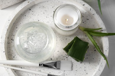 Photo of Jar of natural gel, burning candle, makeup brushes and fresh aloe leaves on white table, top view