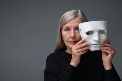 Photo of Multiple personality concept. Woman with mask on gray background, space for text