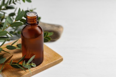 Photo of Bottle of eucalyptus essential oil and plant branches on white table, space for text