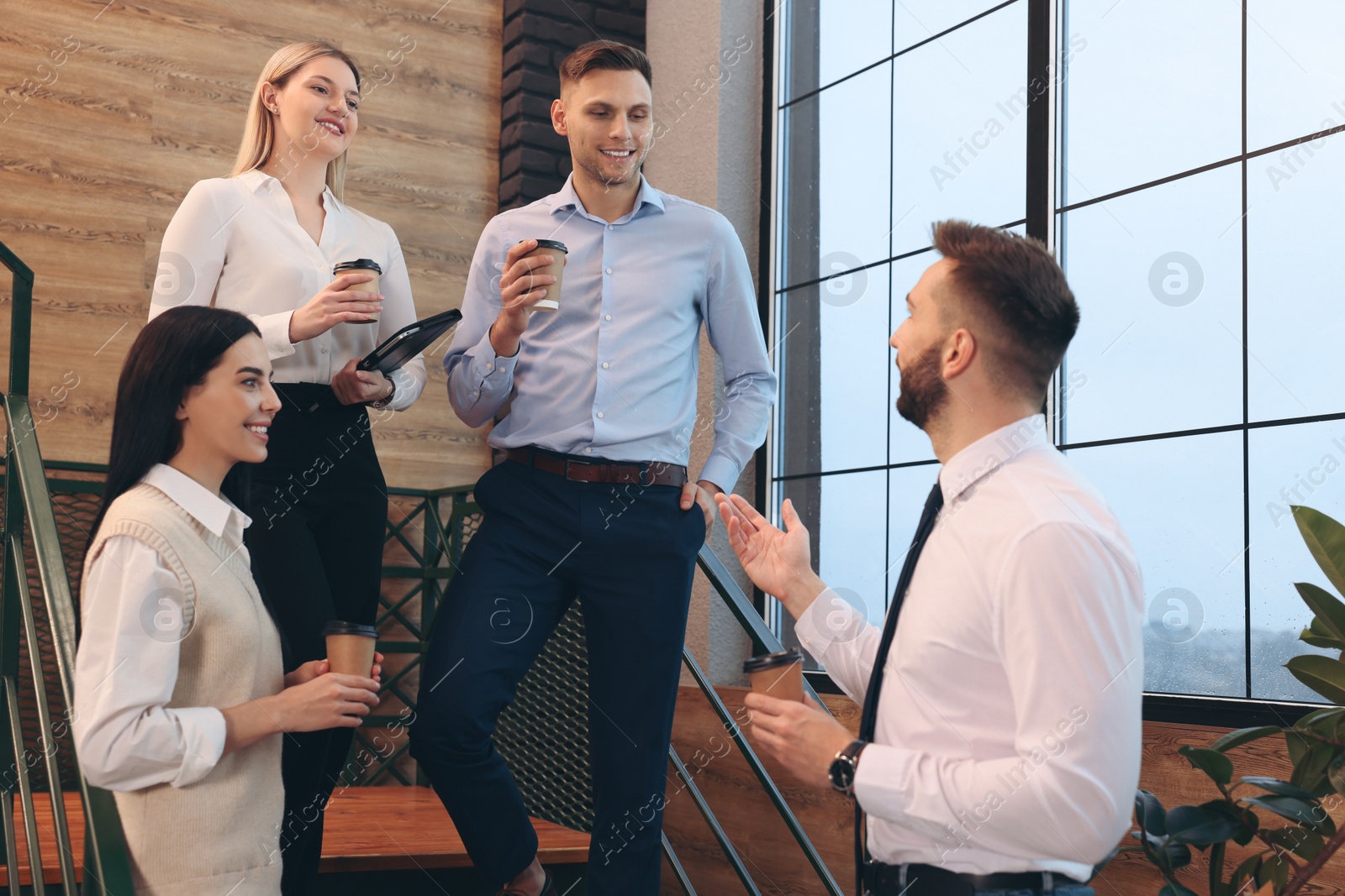 Photo of Group of coworkers talking during coffee break on stairs in office