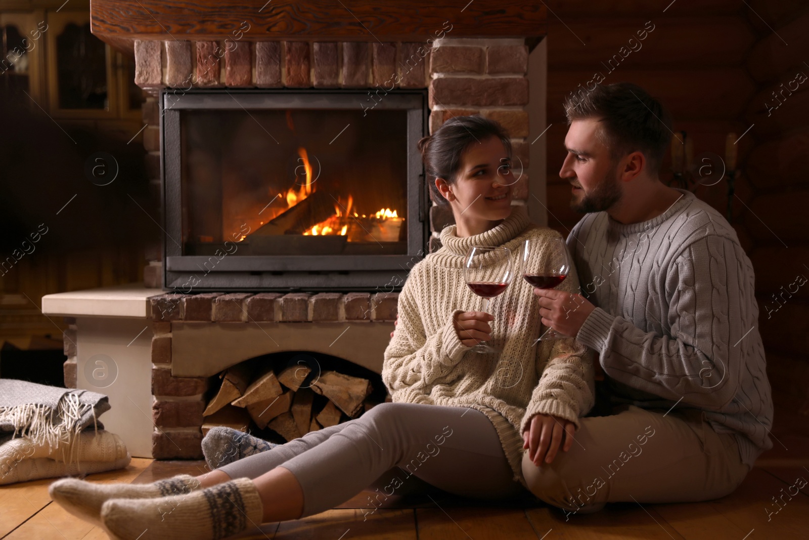 Photo of Lovely couple with glasses of wine near fireplace at home. Winter vacation